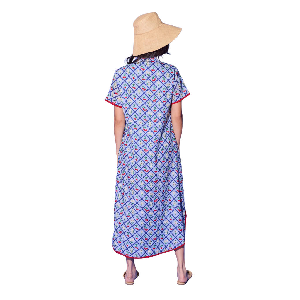 Person wearing a blue patterned dress with a straw hat on a white background