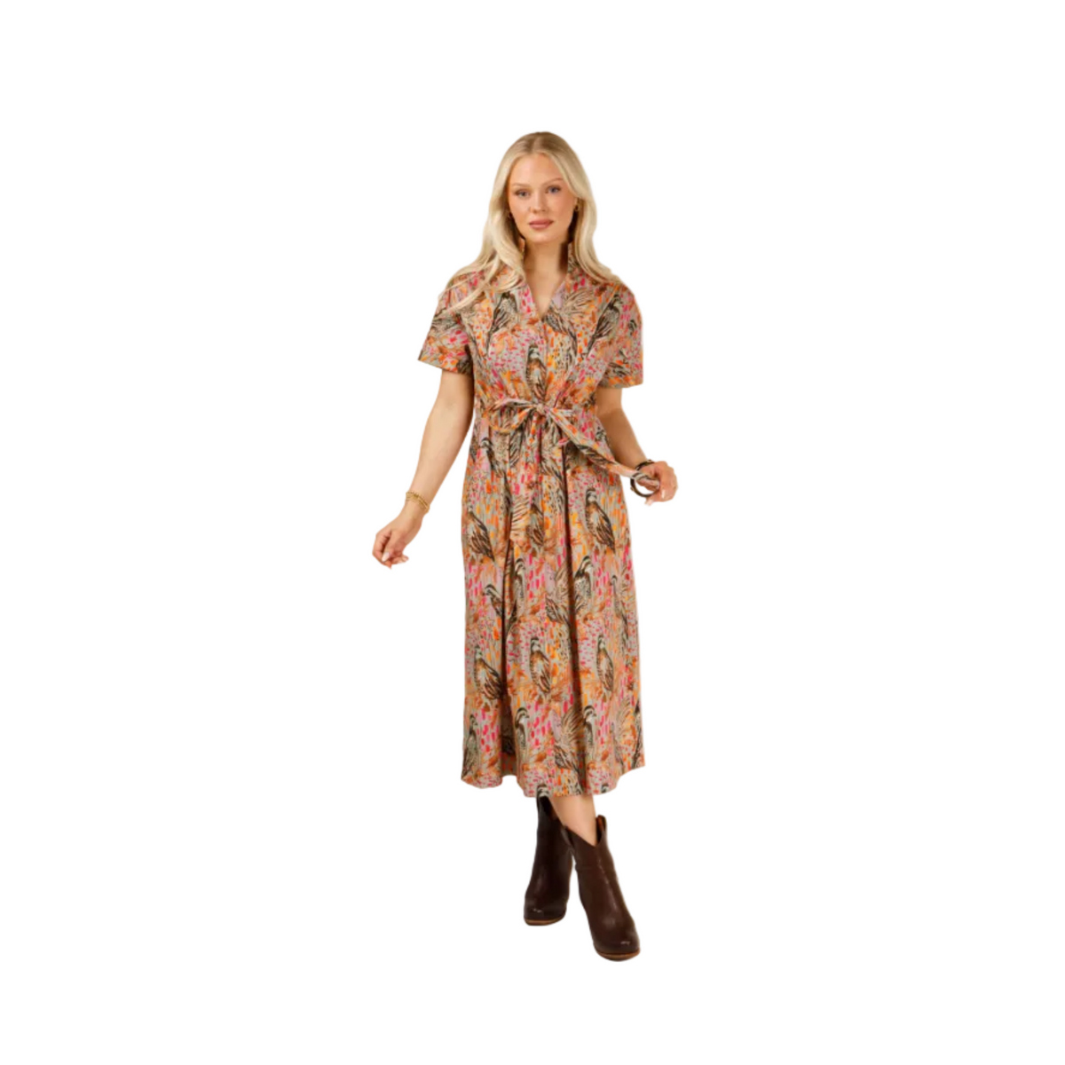 A woman modeling a short-sleeve midi dress with a colorful paisley pattern in pink, orange, and green, featuring a tie waist belt, paired with dark brown ankle boots, against a light gray studio background.