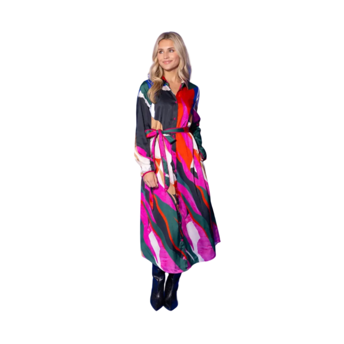 A woman modeling a long-sleeved midi dress with a bold abstract multicolor print, featuring pink, red, green, and white shapes on a black base, paired with black ankle boots, set against a solid blue studio background.