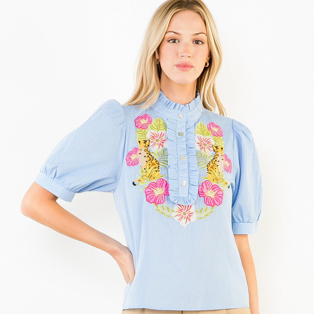 Woman wearing a light blue blouse with floral embroidery and beige shorts on a white background