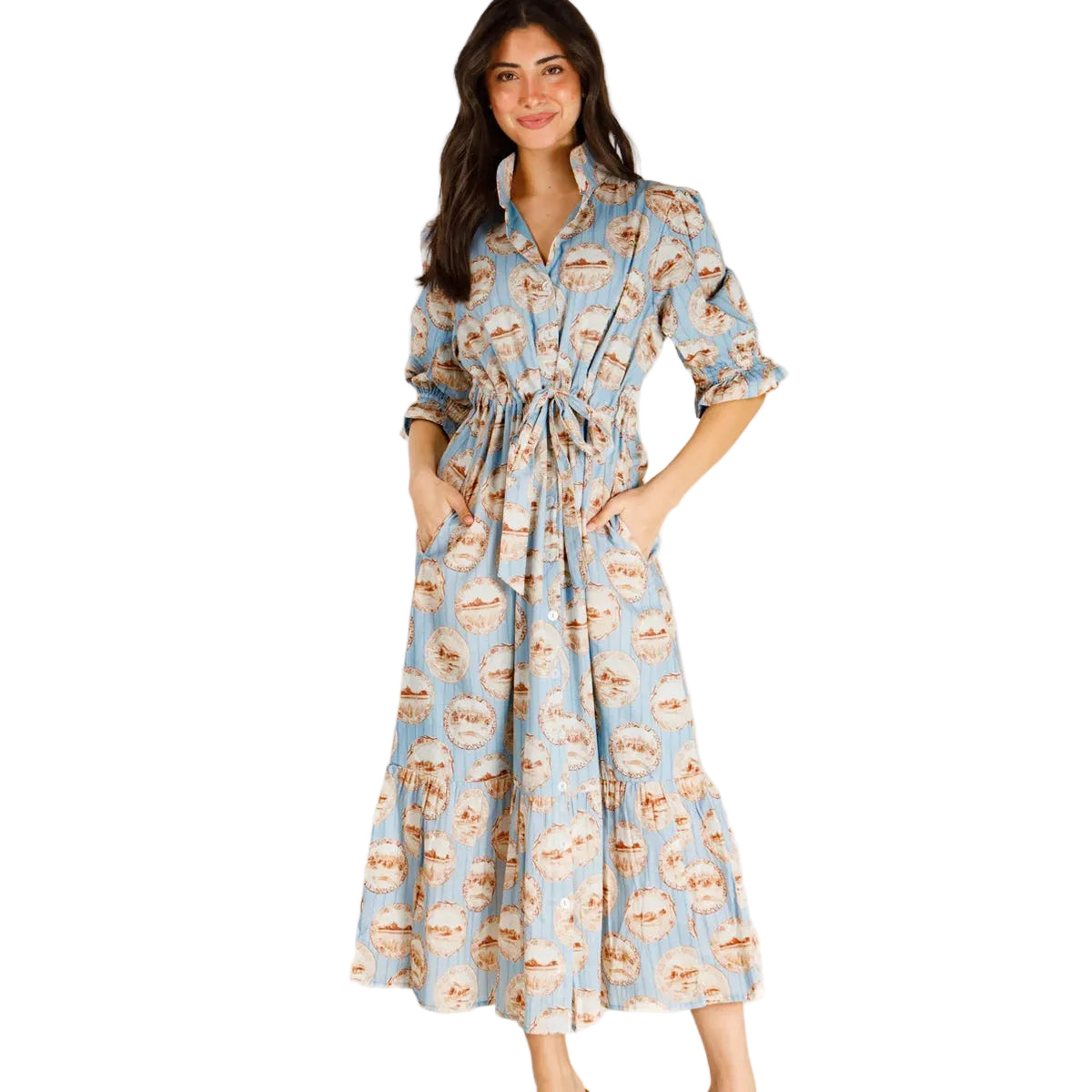 A woman modeling a light blue midi shirt dress with a brown and beige coffee cup pattern, featuring a tie waist and pockets, paired with brown slide sandals against a plain white studio background.
