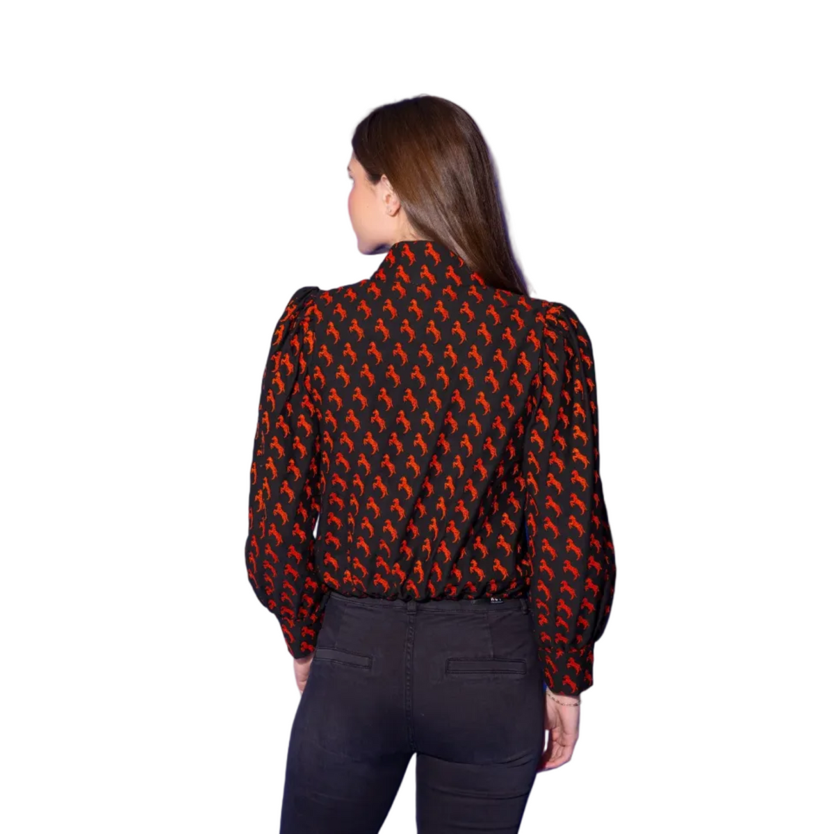 A woman shown from the back wearing a black blouse with a repeating red and orange abstract pattern, paired with dark pants, set against a solid blue studio background.