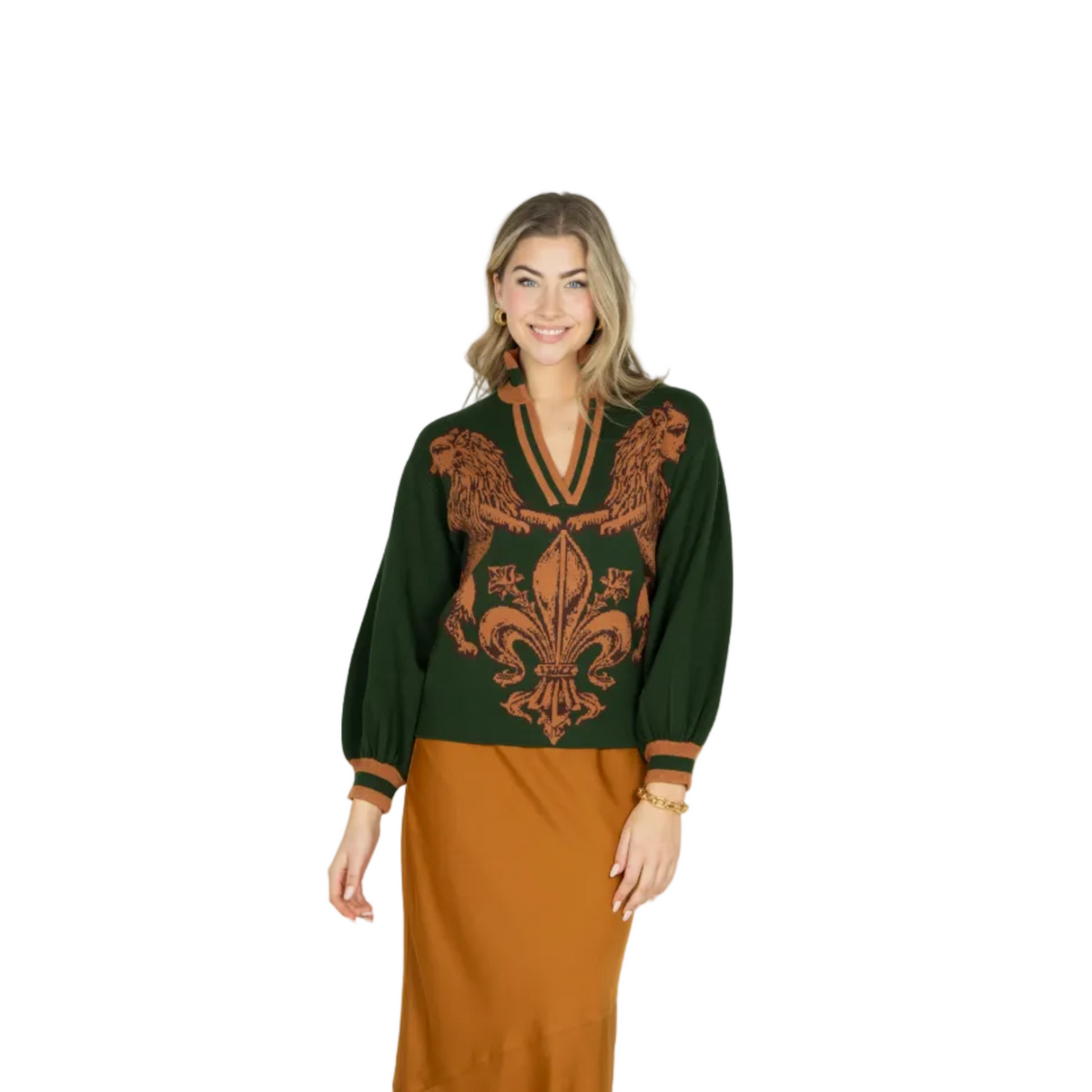 A woman modeling a dark green knit sweater with a large rust-orange baroque-style floral pattern on the front, paired with a rust-orange skirt, against a light gray studio background.