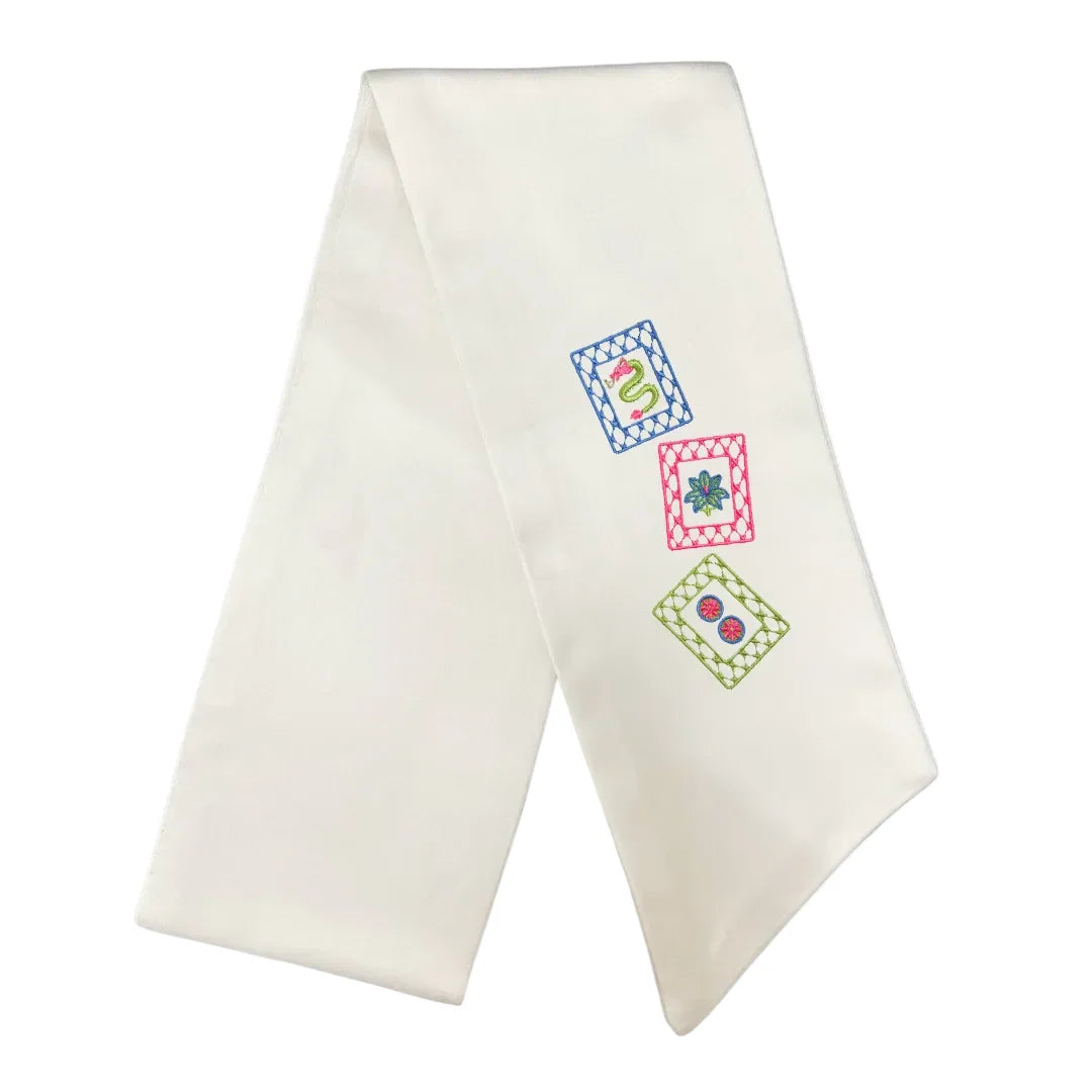 An off-white satin or silk baby baptismal or christening veil with three colorful embroidered monogram squares on the right side, displayed on a clean white background.