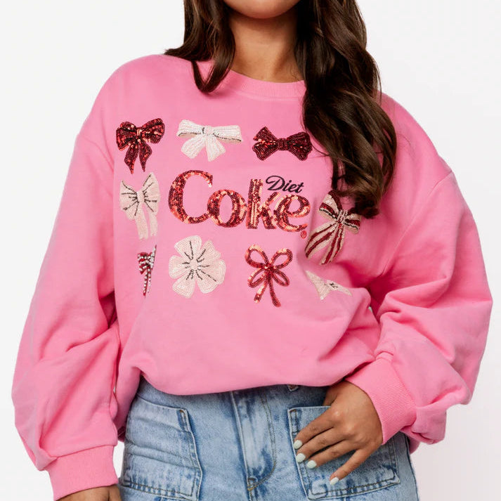 Person wearing a pink sweatshirt with decorative elements and text, standing against a plain background