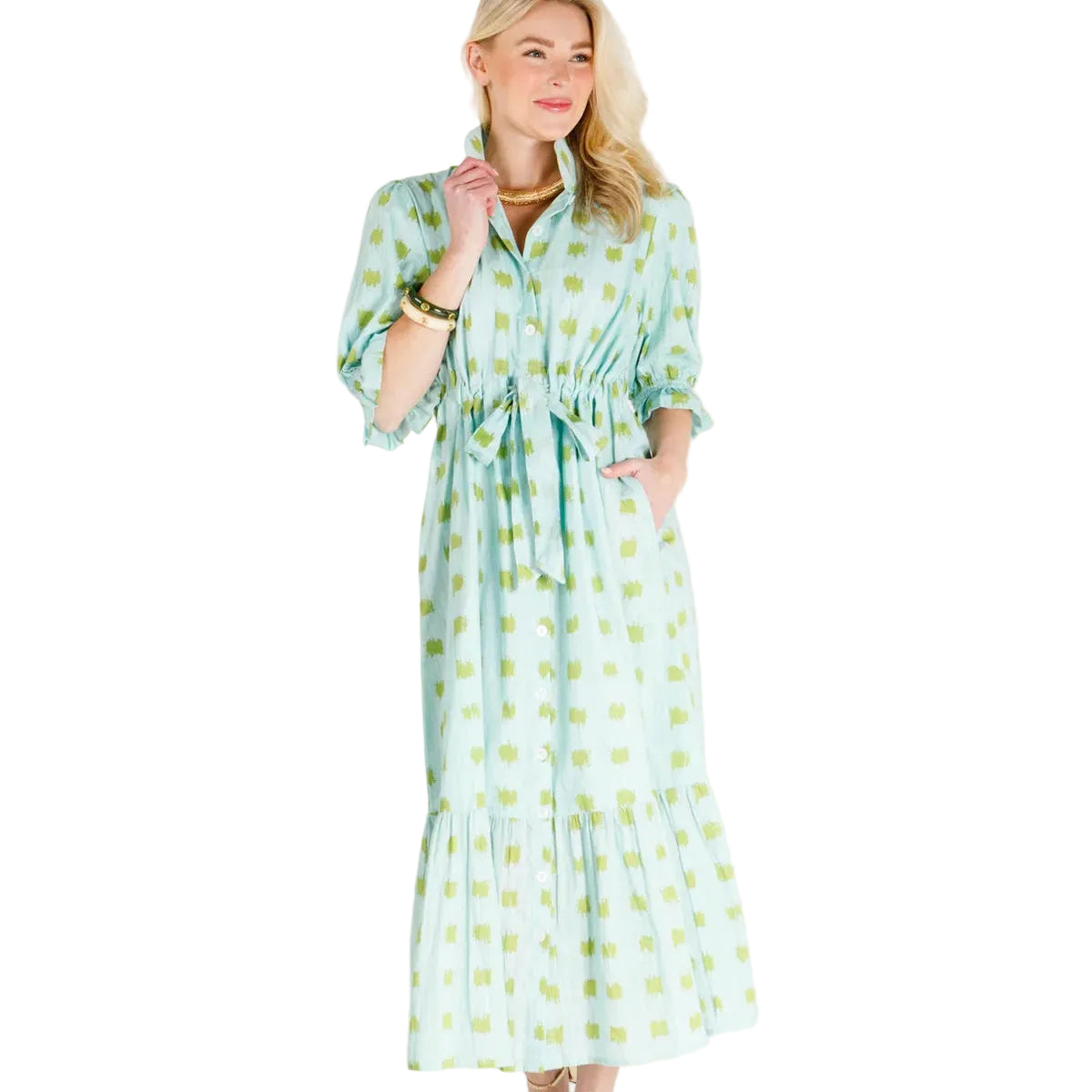 A woman modeling a light green and white patterned midi dress with puff sleeves, a tie waist, and a ruffled hem, standing against a plain white studio background.