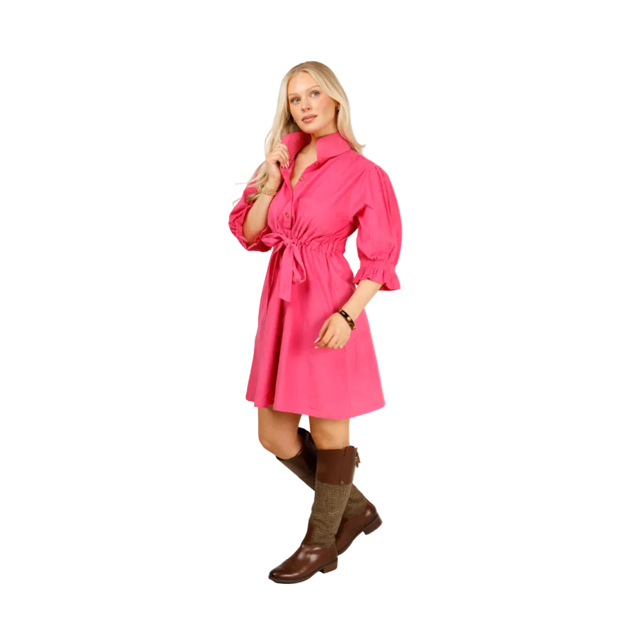 A blonde woman models a bright pink shirt dress with a tie waist and brown knee-high socks with brown boots, standing against a light gray studio background.