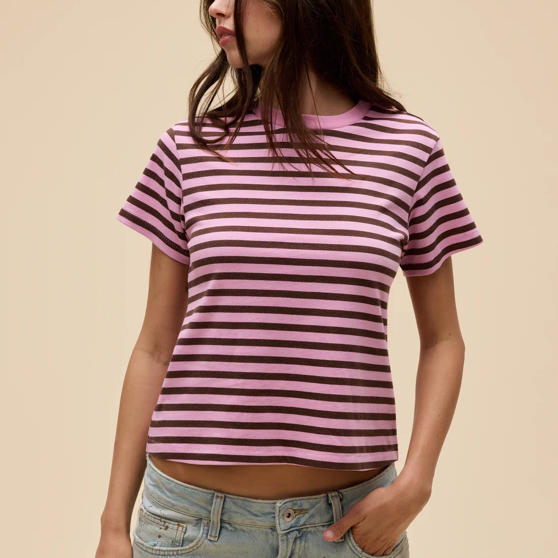 Person wearing a pink and purple striped t-shirt with light blue jeans on a beige background