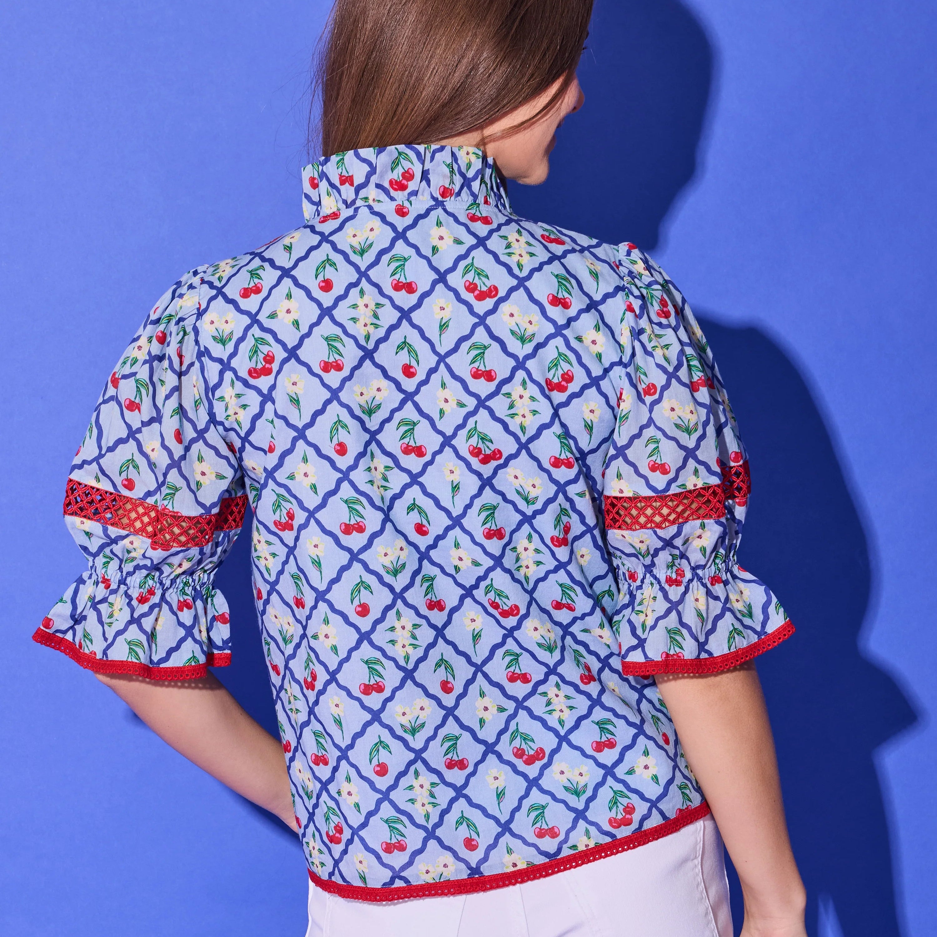 Person wearing a patterned shirt and white shorts against a blue background