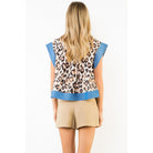 A woman shown from the back wearing a sleeveless leopard-print top with bright blue ribbed trim and beige shorts against a plain white studio background.