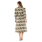 A woman viewed from the back wearing a long-sleeve midi dress with a repeating tree print on a cream background. The dress has a dark olive green and brown tree motif.