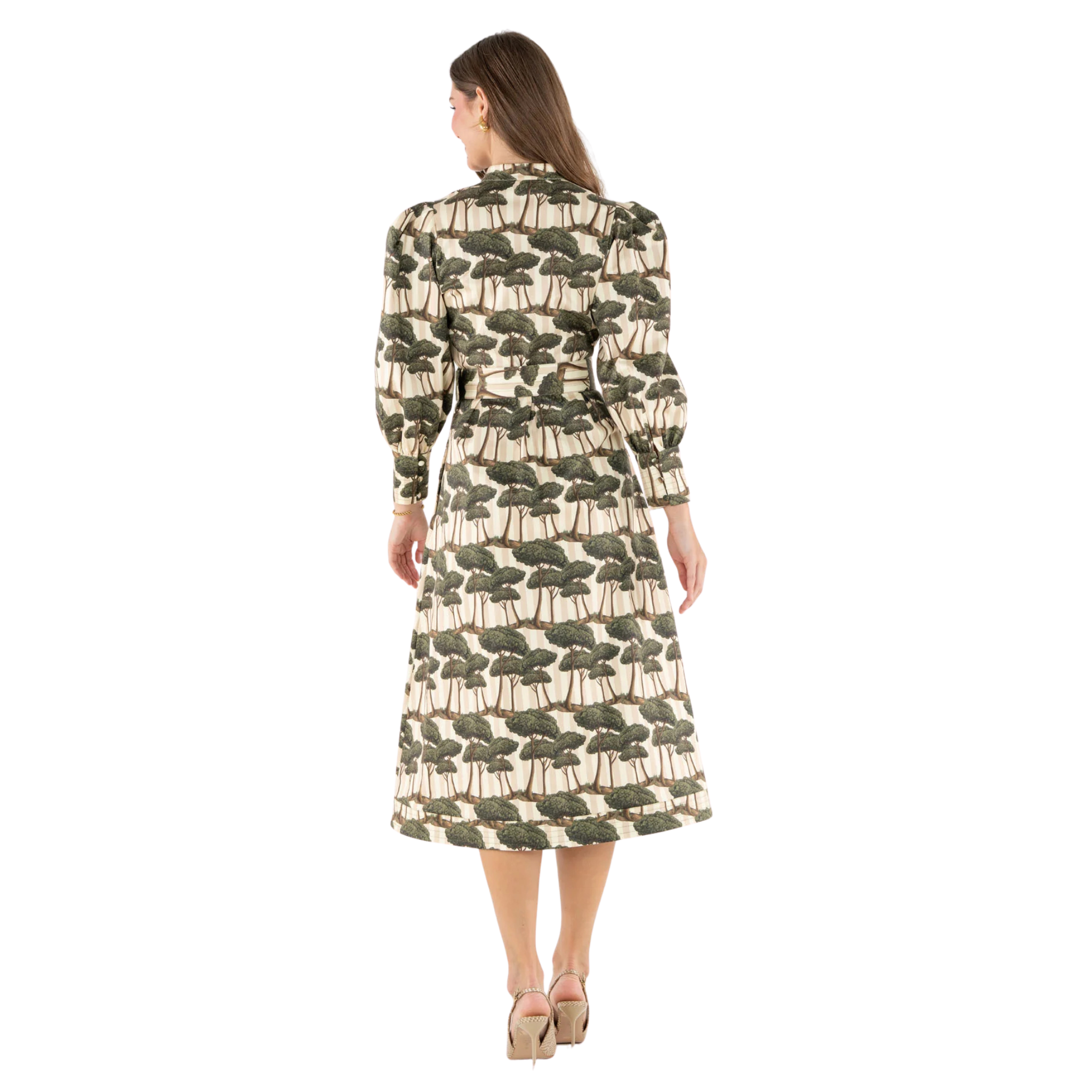 A woman viewed from the back wearing a long-sleeve midi dress with a repeating tree print on a cream background. The dress has a dark olive green and brown tree motif.