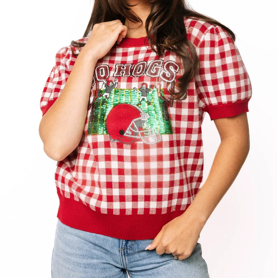 Woman wearing a red and white checkered shirt with 'Hogs' and a logo, standing against a white background.