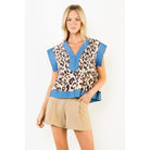 A woman modeling a short-sleeve knit top with a beige, brown, and black leopard print pattern, accented with bright blue trim on the V-neck, sleeve cuffs, and hem, paired with tan shorts against a plain white background.