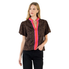 A woman modeling a short-sleeve brown leopard-print blouse with a vibrant pink and orange striped split neckline, paired with black pants, against a plain white background.