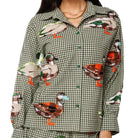 A woman wearing a matching long-sleeve button-up shirt and shorts pajama set in a green and white gingham pattern, decorated with realistic embroidered ducks in various colors.