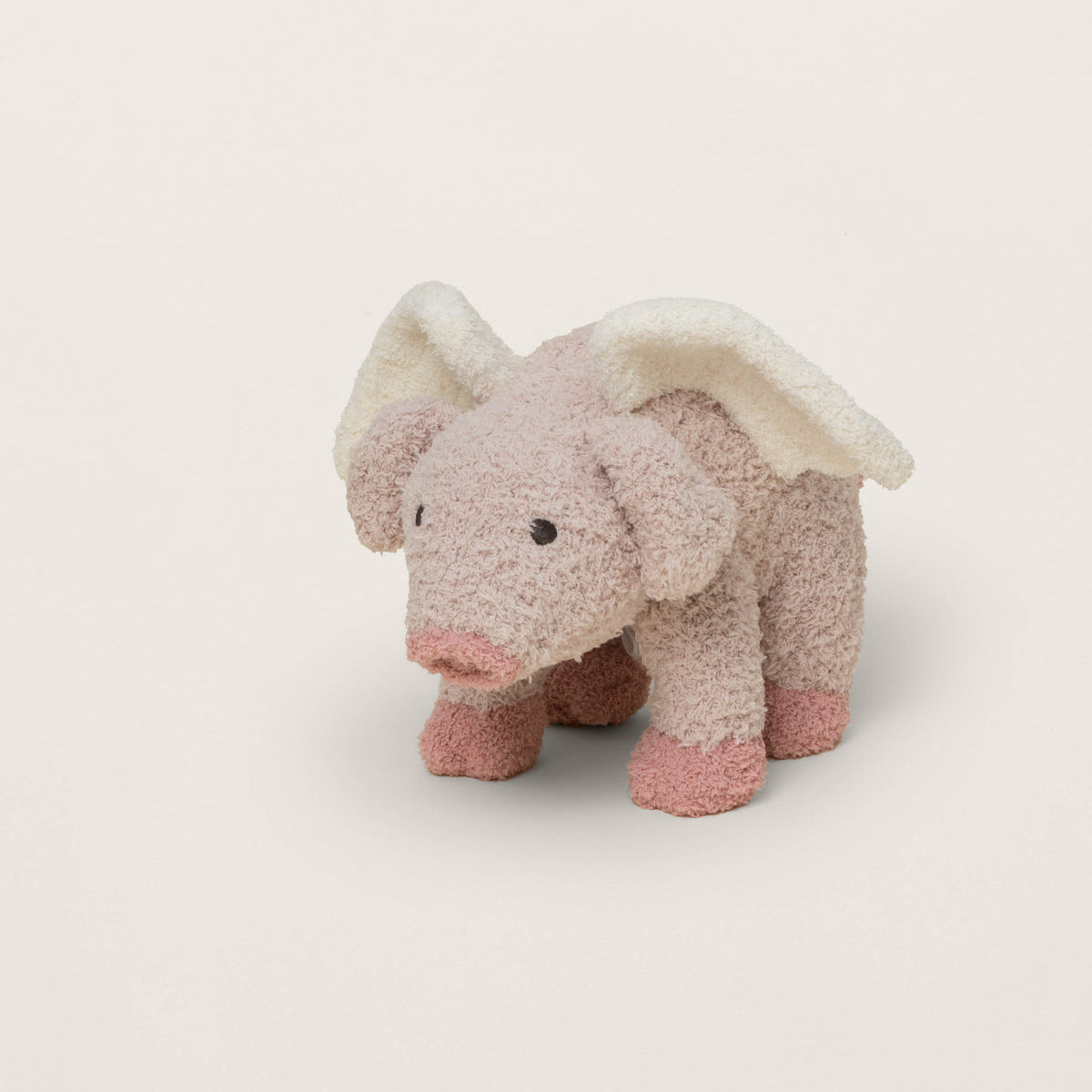 Plush toy elephant with pink feet and white wings on a light beige background