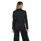 A woman shown from the back wearing a black tailored blazer with gold button accents on the sleeves and matching black trousers, photographed against a light gray studio background.