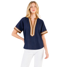 A woman modeling a short-sleeve navy blue top with tan and white trim on the V-neck and sleeve cuffs, paired with white pants, against a plain white background.