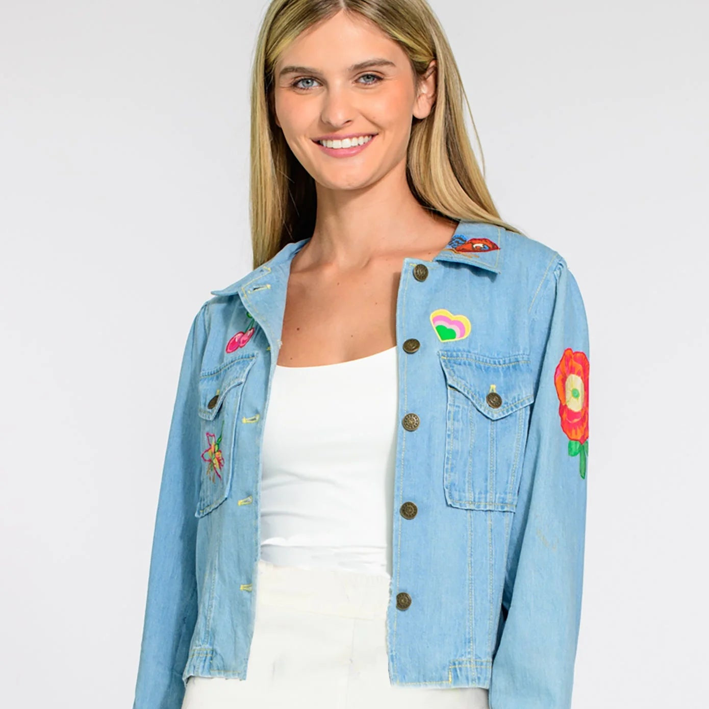 Woman wearing a light blue denim jacket with colorful patches on a white background