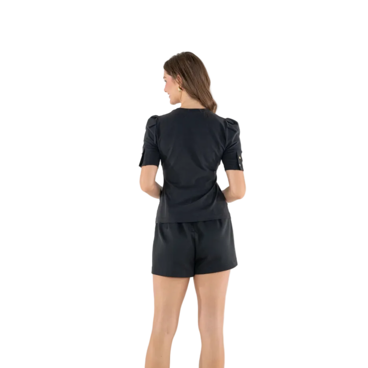 A woman viewed from the back wearing a black short-sleeve top with puffed shoulders and matching black shorts, photographed against a plain light gray studio background.