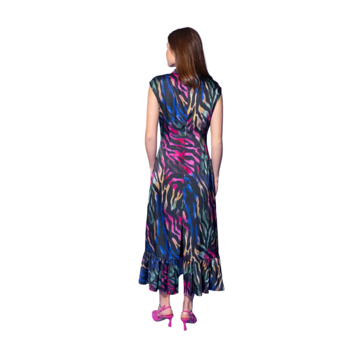 A woman modeling a sleeveless, high-neck midi dress with a colorful abstract print in pink, green, blue, and yellow on a black base, paired with bright pink heels, set against a solid blue studio background.