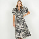 A woman modeling a black and white geometric print midi dress with puff sleeves and a V-neckline, standing against a plain white studio background.