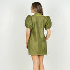 A woman viewed from the back wearing a short olive green mesh puff-sleeve dress with a high collar, paired with beige high-heeled sandals, against a plain white studio background.