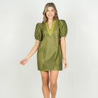A woman modeling a short olive green puff-sleeve dress with a textured, dotted mesh-like pattern and a V-neckline, set against a plain white studio background.