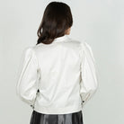 A woman shown from the back wearing a white cropped jacket with puffed long sleeves and a black skirt, against a plain light gray studio background.