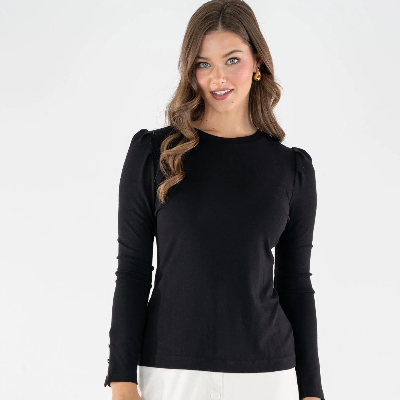 A woman modeling a black long-sleeve top with puffed shoulders and a crew neckline, paired with a white skirt, against a plain white studio background.