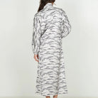 A woman viewed from behind wearing a long-sleeved collared shirt dress with a black and white zebra-like abstract pattern, paired with black flat sandals, against a plain white studio background.