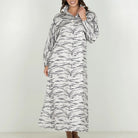 A woman modeling a long-sleeved maxi dress with a black and white zebra print pattern, standing against a plain light gray studio background.