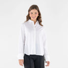A woman modeling a white long-sleeve button-up blouse with a high stand collar and black wide-leg trousers, photographed against a plain light gray studio background.