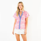 Woman wearing a pink and white patterned blouse with white shorts on a white background