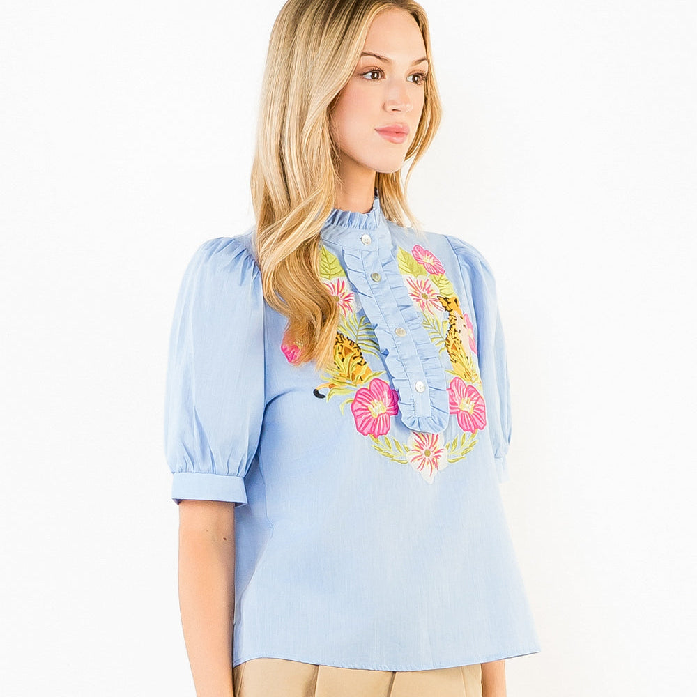 Woman wearing a light blue blouse with floral embroidery and beige shorts on a white background
