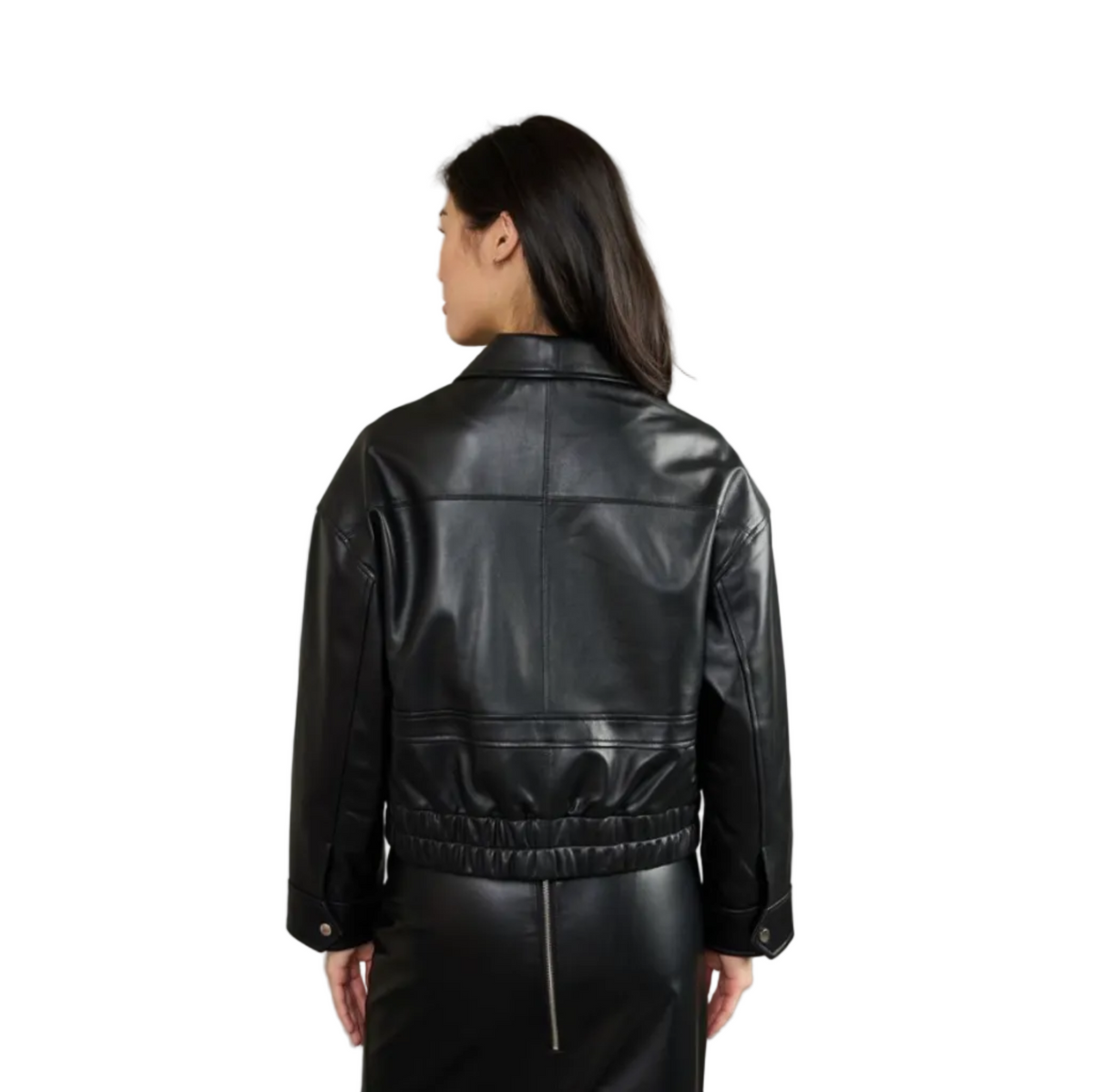 A woman shown from the back wearing a black leather cropped jacket with a gathered elastic waist and button cuffs, paired with a black skirt, against a solid gray studio background.