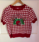 A red and white gingham knit crewneck sweater with a 'GO HOGS' football graphic on the front, hanging on a wooden hanger against a white paneled door.