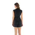 A woman shown from the back wearing a sleeveless black vest and matching black shorts against a plain light gray studio background.