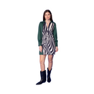 A model stands against a solid blue studio background wearing a long-sleeve collared mini dress with a green yoke and a black-and-white zebra patterned center panel, paired with black cowboy boots.