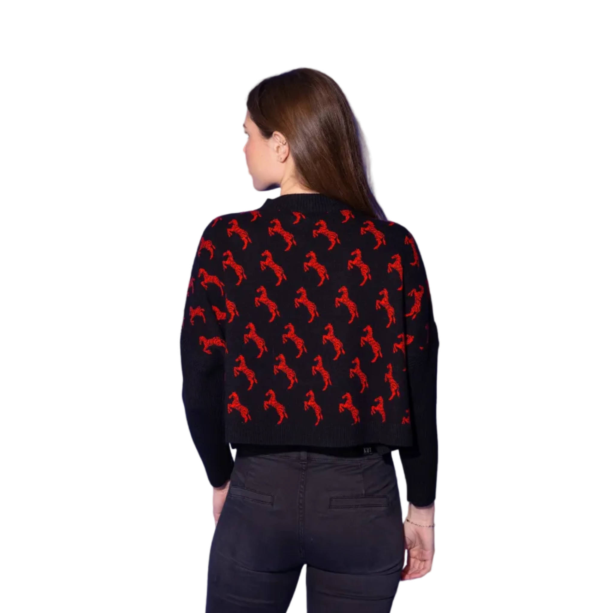 A woman shown from the back wearing a black cropped sweater with a repeating red horse pattern, paired with dark gray jeans, set against a solid blue studio background.