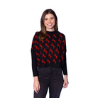 A woman modeling a black long-sleeve knit sweater with a repeating red horse pattern, paired with black jeans, set against a solid blue studio background.
