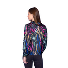 A woman shown from the back wearing a long-sleeve satin blouse with a vibrant multicolor abstract pattern, set against a solid blue studio background.