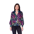A woman modeling a long-sleeve satin blouse with a vibrant multicolor abstract print, paired with black pants, set against a solid blue studio background.