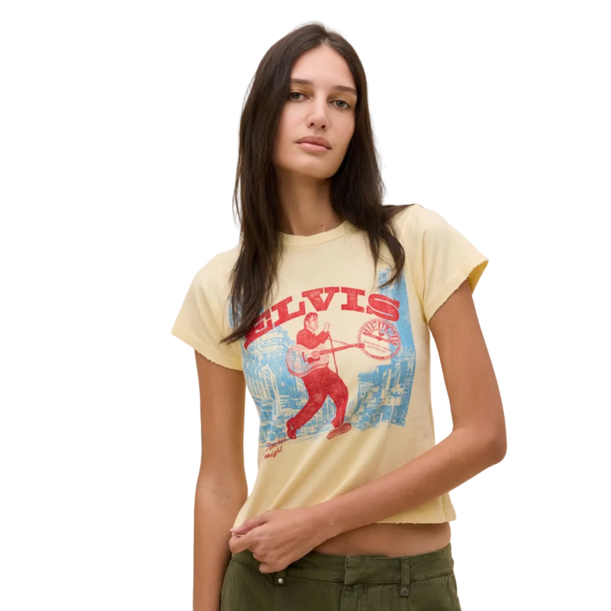 A woman modeling a cropped cream-colored graphic t-shirt featuring a red and blue Elvis Presley design, paired with olive green pants, against a solid beige background.