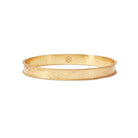 A hammered gold bangle bracelet with a twisted rope border and a small hexagonal logo mark on the inside, shown on a clean white background.