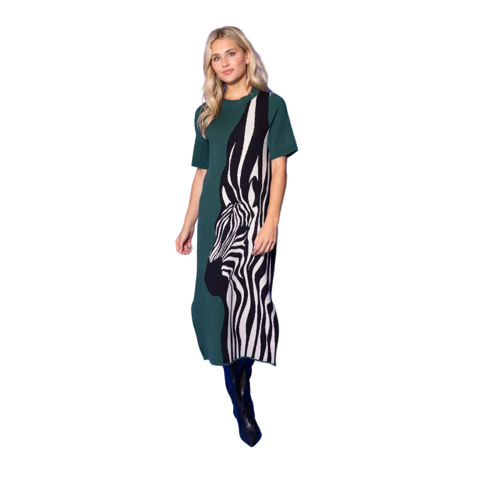 A woman modeling a short-sleeve knit dress with a color-blocked design in dark green and a zebra print panel, paired with black boots, set against a solid blue studio background.