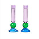 Two matching translucent glass candlestick holders with purple cylindrical upper sections, green spherical middle sections, and blue circular bases, shown on a plain white background.