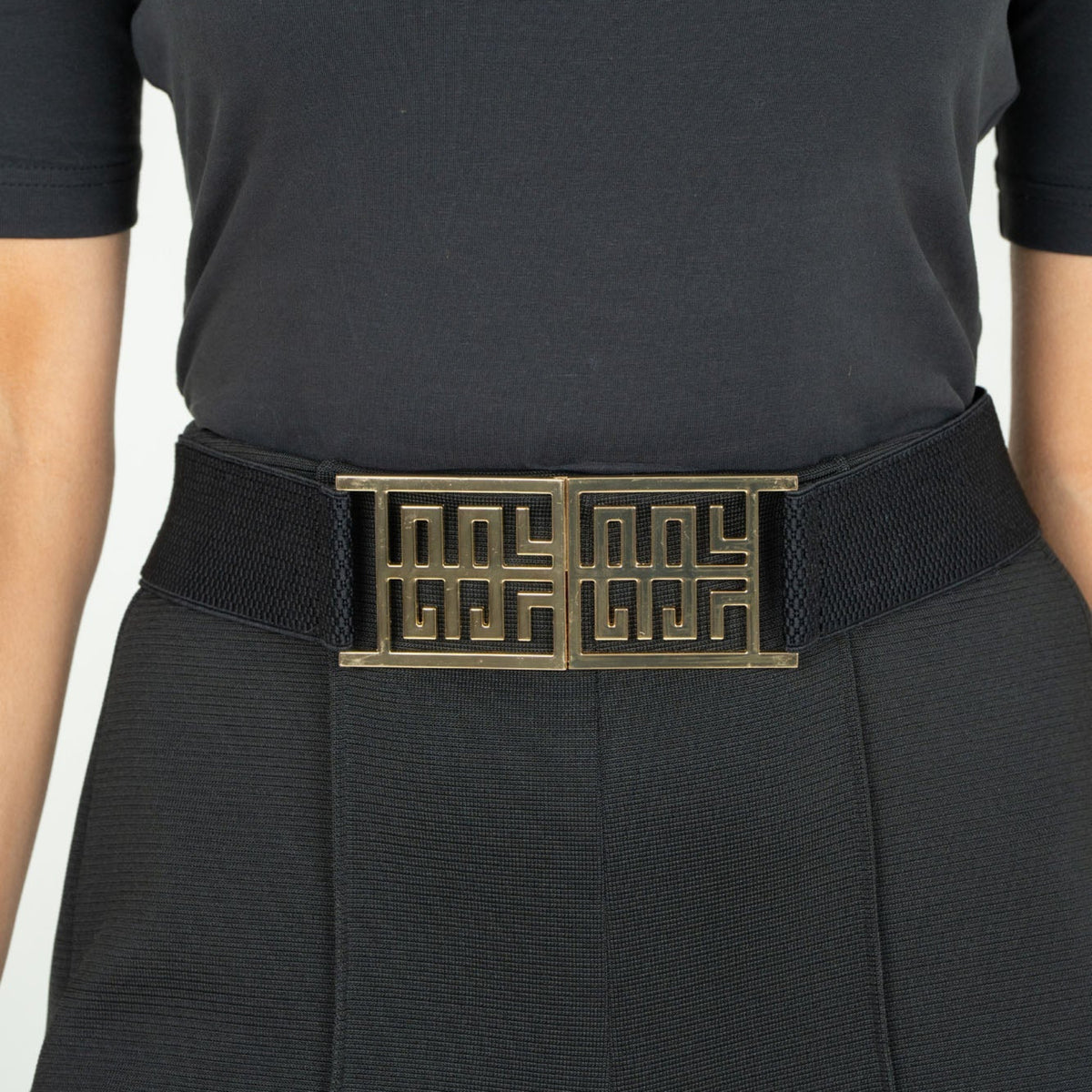 Person wearing a black belt with a gold buckle on a plain background
