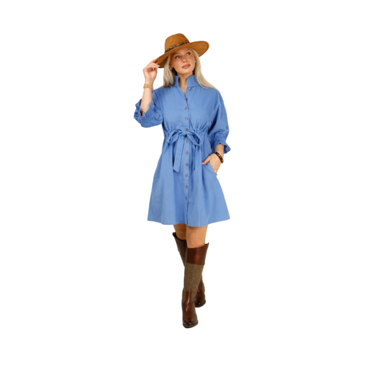 A woman modeling a blue button-front shirt dress with a tie waist, styled with a brown wide-brim hat, brown boots, and brown knee-high socks against a light gray studio background.